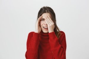 Woman wearing a red sweater is covering half of her face with her hand and shielding the other half with her other hand in embarrassment 